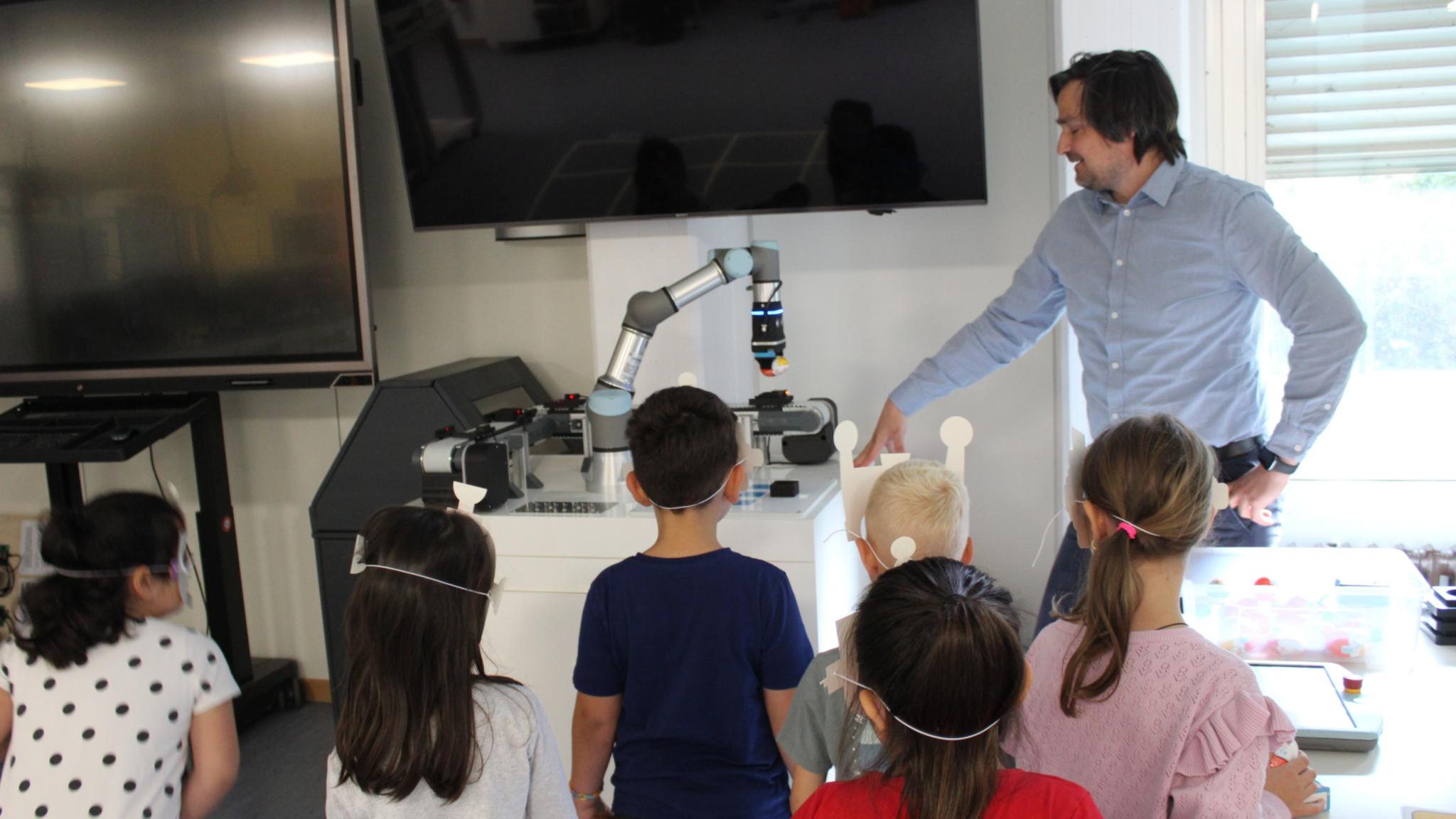 Kinder gucken einem Roboterarm zu, der ein Überraschungsei transportiert.