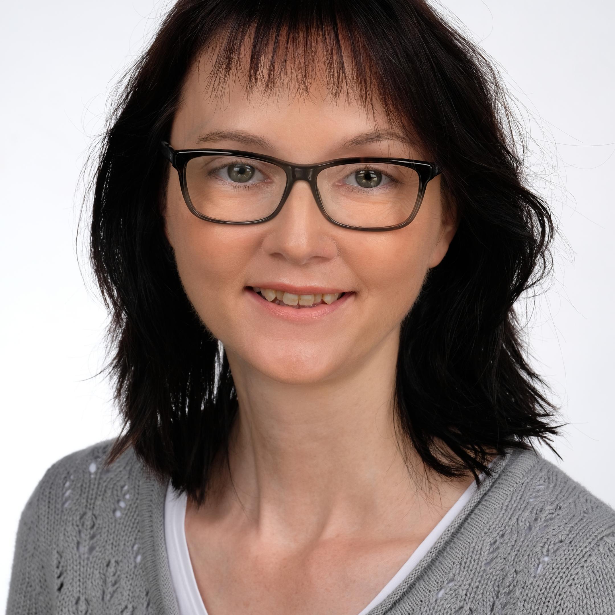 Eine Frau mit dunklen Haaren, einer schwarzen Brille und einer grauen Strickjacke