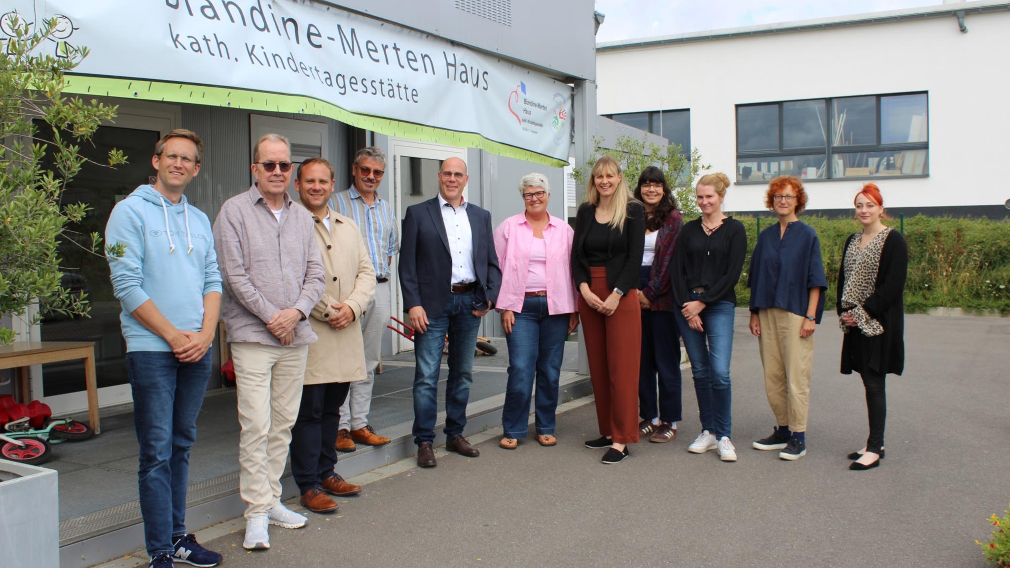 Eine Reihe von Männern und Frauen, die vor einer weißen Container-Kita stehen.