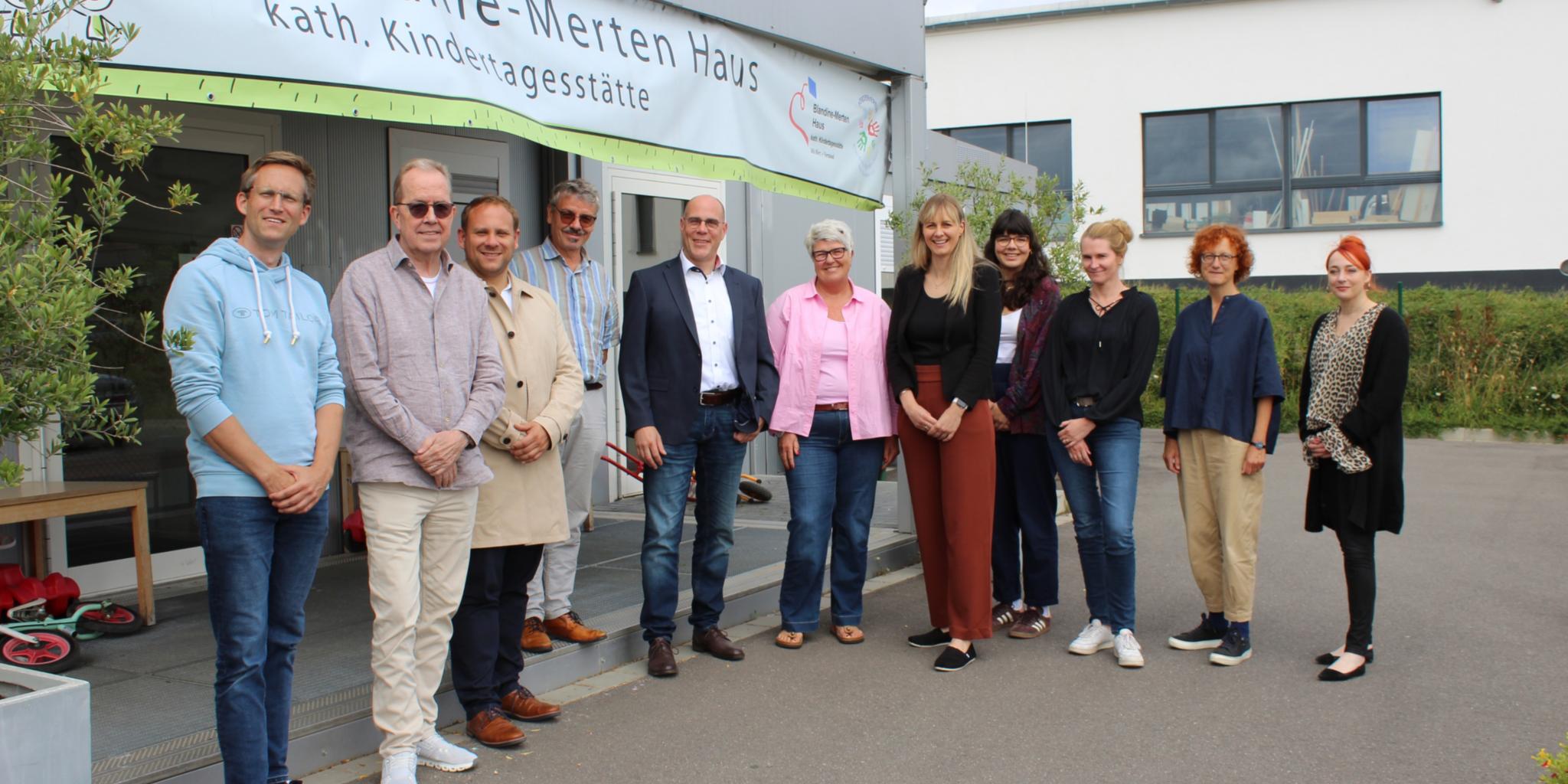 Eine Reihe von Männern und Frauen, die vor einer weißen Container-Kita stehen.